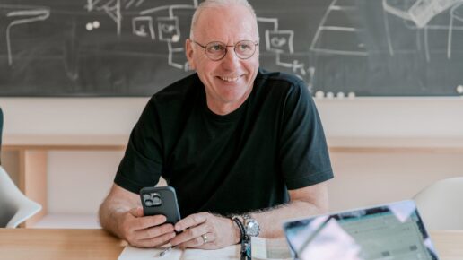 Smiling Vetica expert with smartphone and notebook in front of a chalkboard.