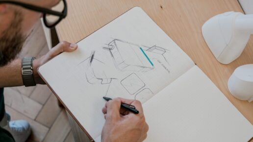 Hand drawing product sketches in a notebook on a wooden table.