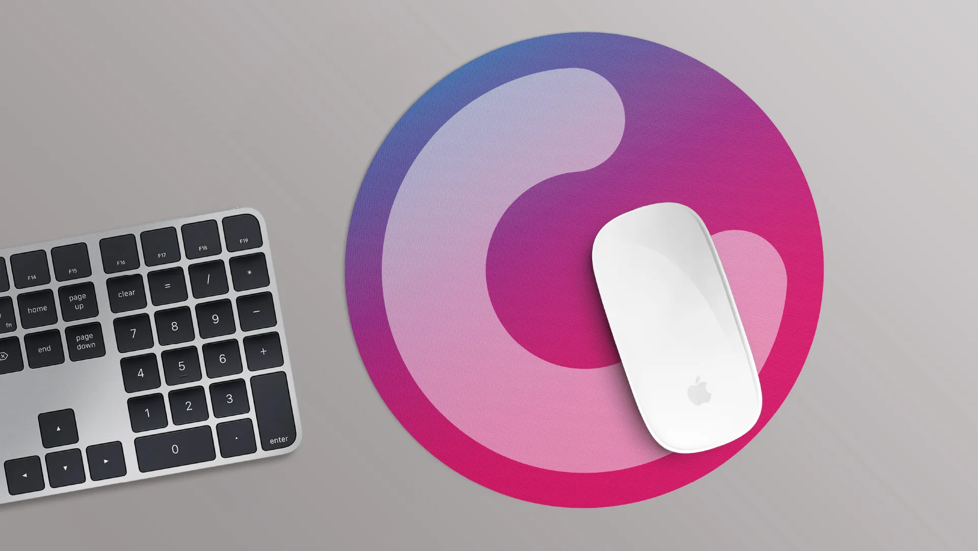 Weisse Apple-Maus auf rundem pink-lila Mauspad neben silberner Tastatur Draufsicht