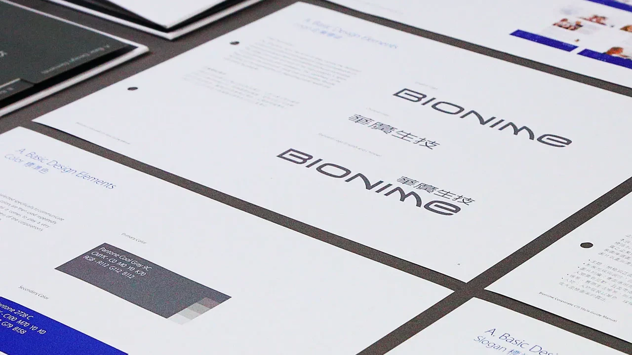 Gedruckte Seiten eines Styleguides mit Logo-Spezifikationen, Farbwerten (Pantone, CMYK) und Slogan-Richtlinien auf einem grauen Tisch.