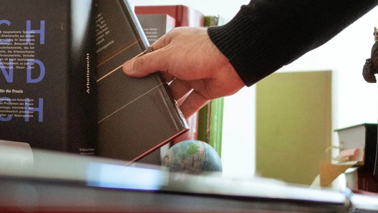 Close-up of a male hand pulling a dark hardcover book titled 