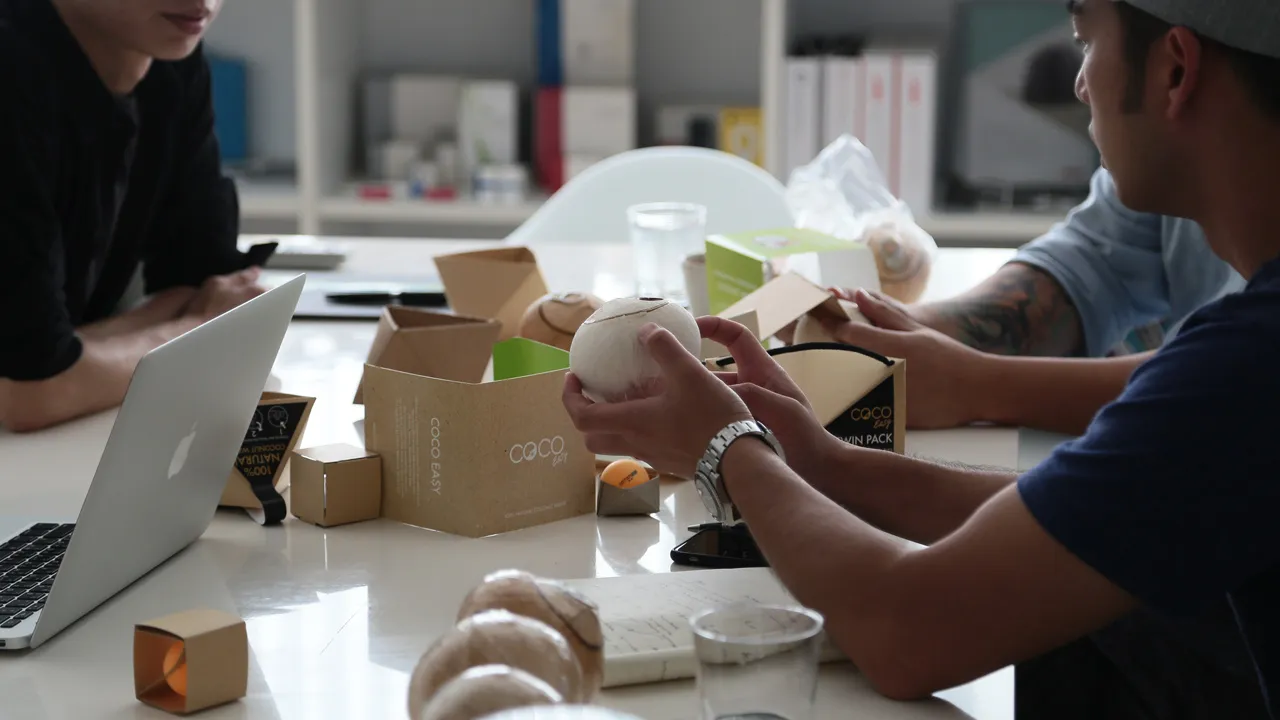 Designers sitting at a table evaluating various cardboard packaging prototypes for the coconuts, including single and twin packs.