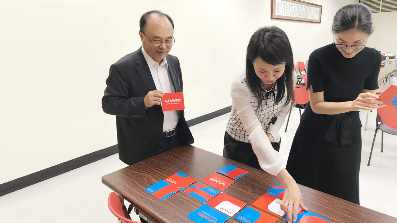 Zwei Vetica-Beraterinnen und ein LIWIN-Manager stehen an einem Tisch und legen rot-blaue Karten mit dem LIWIN-Logo in einem Muster aus.
