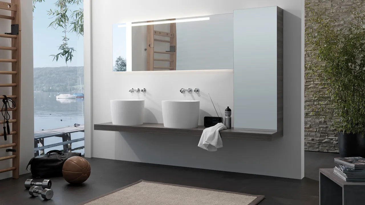 An open space concept featuring wall bars, weights, and a bathroom area with round white vessel sinks on a dark wooden console.