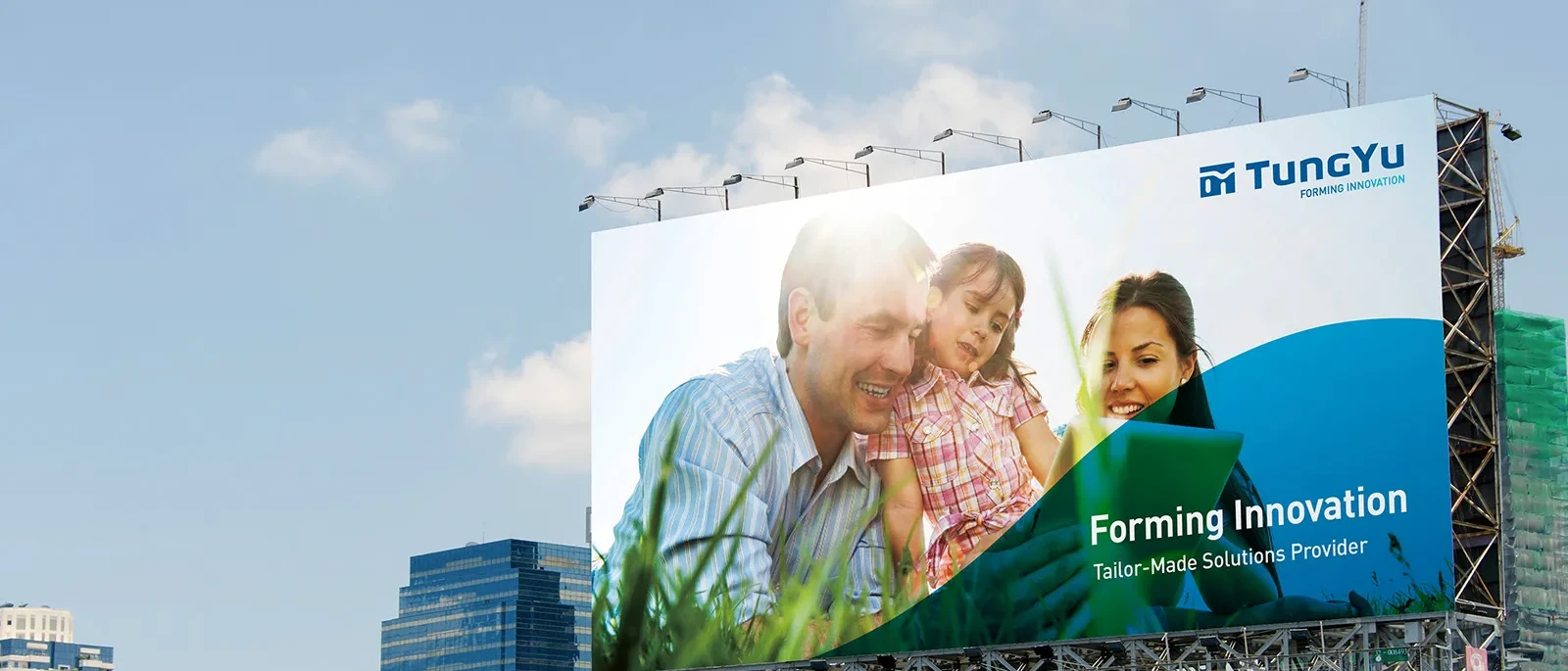 Grosses Werbeplakat an einer Metallkonstruktion vor blauem Himmel mit einer gluecklichen Familie im Gras, dem TungYu Logo und dem Kampagnenslogan.