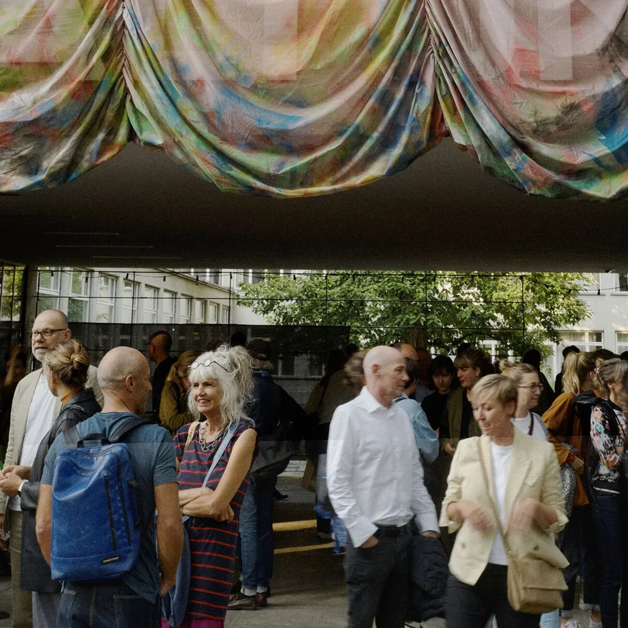 Grosse Gruppe von Besuchern unterhaelt sich unter einem farbenfrohen Stoffbaldachin am Eingang des Museums waehrend der Zurich Design Weeks.